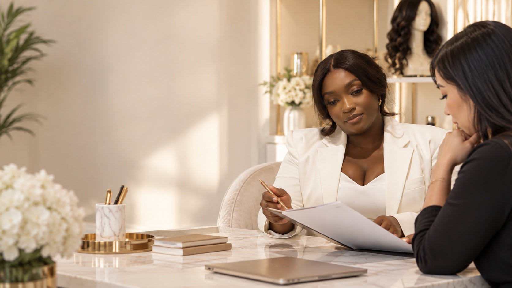 Two women reviewing documents together at a marble desk in a bright ivory and gold room